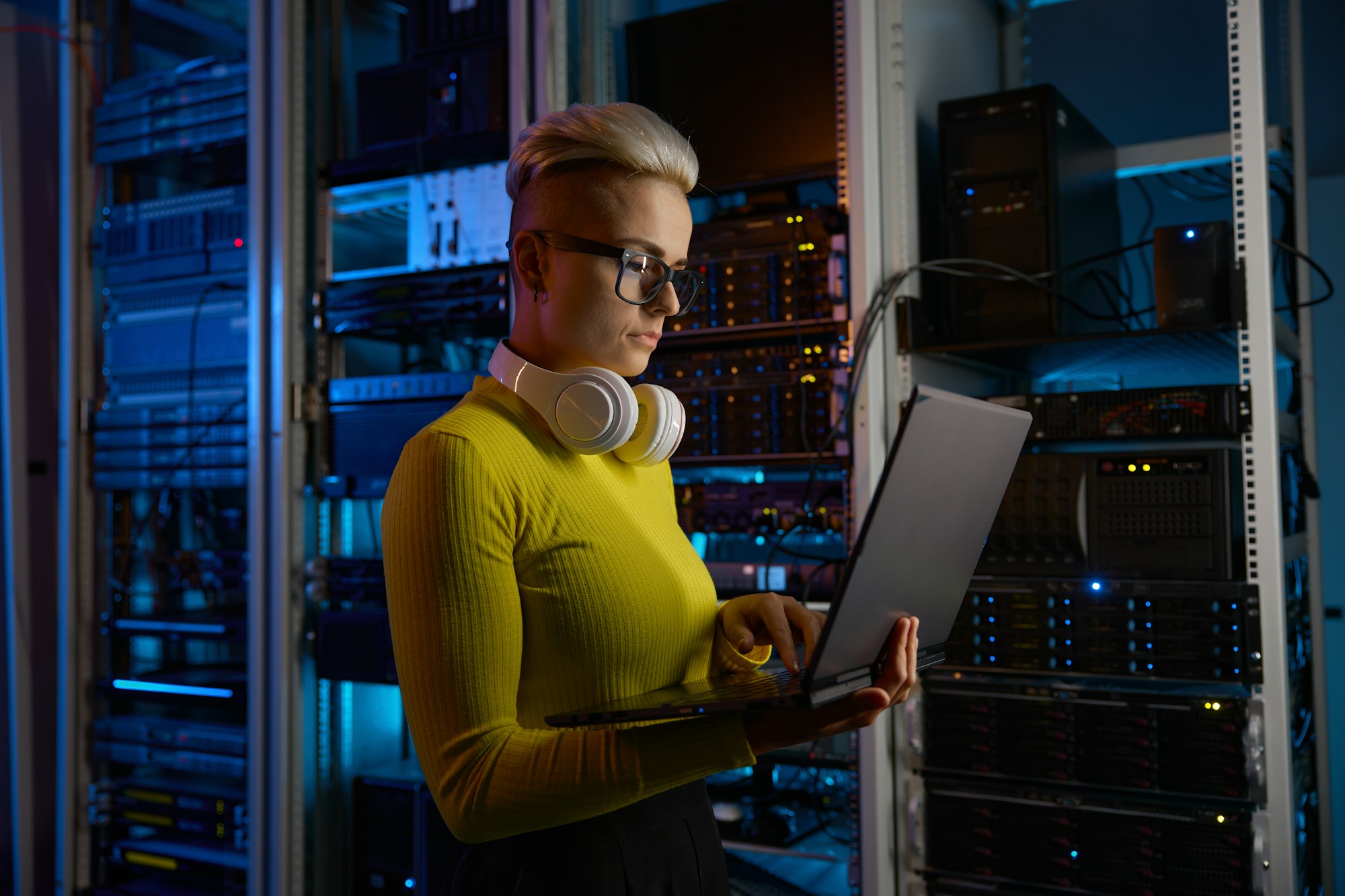 Side view of woman engineer working on laptop at network equipment